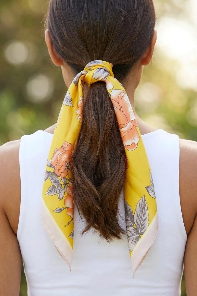 Woman with a yellow floral scarf tied around her ponytail against a blurred natural background
