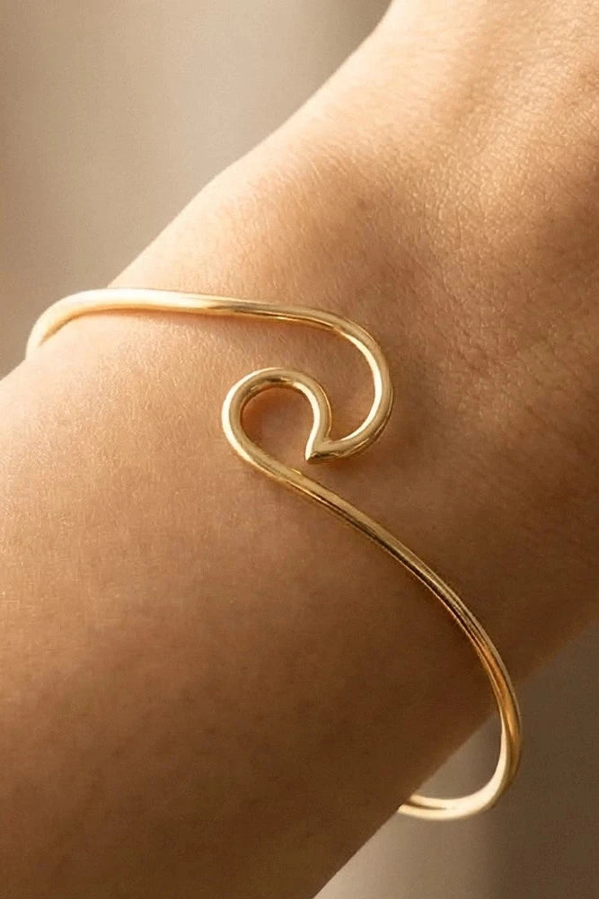 Gold wave-shaped bracelet on a wrist with a neutral background