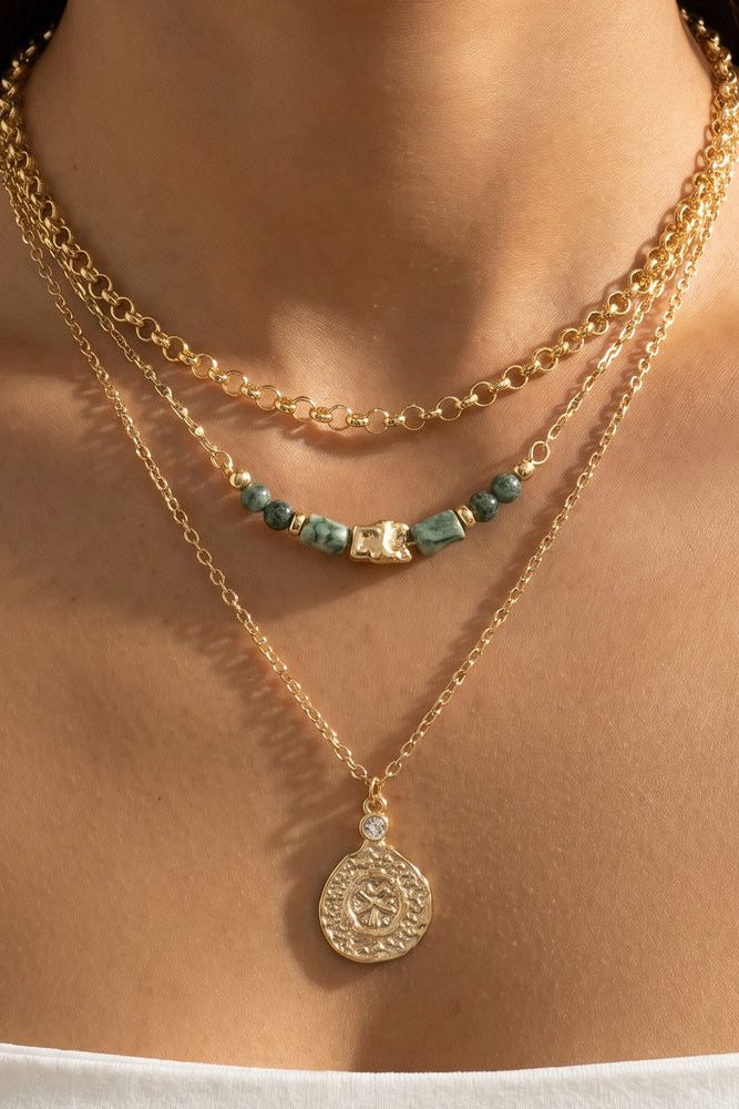 Close-up of a person wearing two gold necklaces with a coin pendant and turquoise beads.